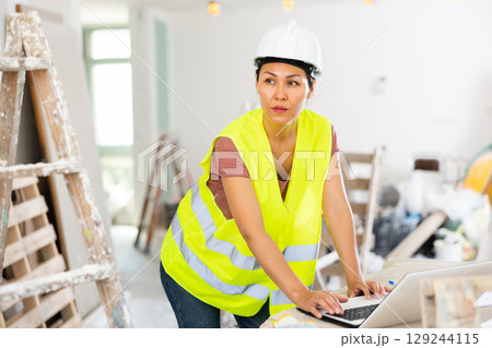 Woman builder using laptop in construction site Woman builder using laptop in construction site 129244115