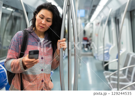 Woman passenger using phone in subway car Woman passenger using phone in subway car 129244535