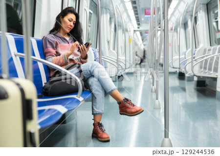 Woman with suitcase sitting in subway car and using her smartphone Woman with suitcase sitting in subway car and using her smartphone 129244536