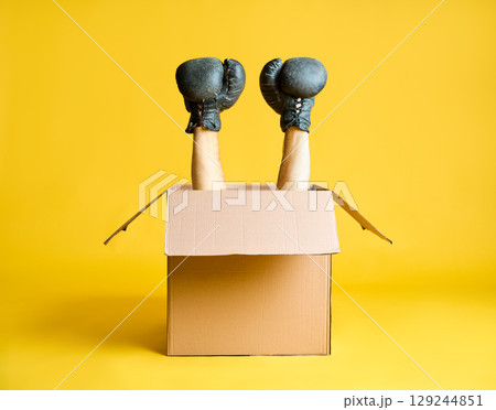 Pair of hands in boxing gloves raised up from open cardboard box Pair of hands in boxing gloves raised up from open cardboard box 129244851