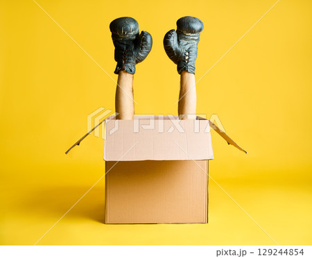 Pair of hands in boxing gloves raised up from open cardboard box 129244854