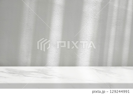White marble table with a white stucco wall texture background featuring natural light beams and shadows 129244991