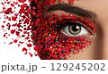 Woman with eye makeup decorated with red glitter and confetti creating a vibrant, artistic look 129245202