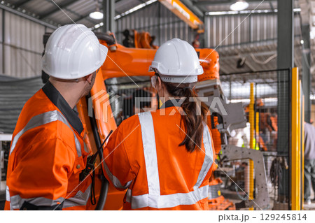 Robotic technician engineer male training helping young women team control operate robot welding arm Robotic technician engineer male training helping young women team control operate robot welding arm 129245814