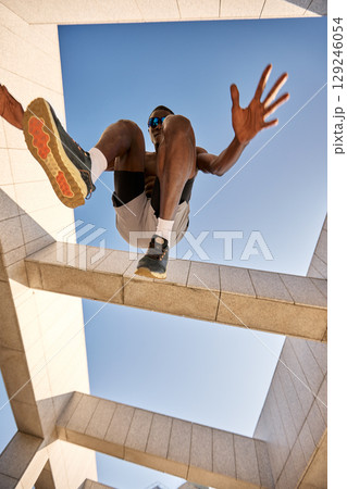 Dynamic athlete performing jump exercise against modern architectural structure and clear sky 129246054