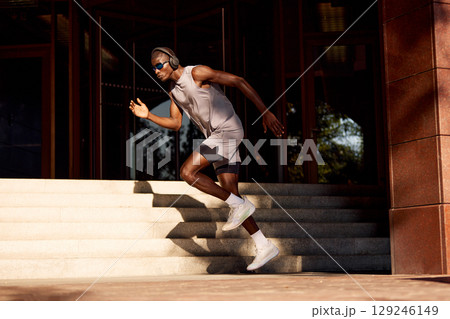 Athletic man running outdoors next to building in evening sunlight 129246149