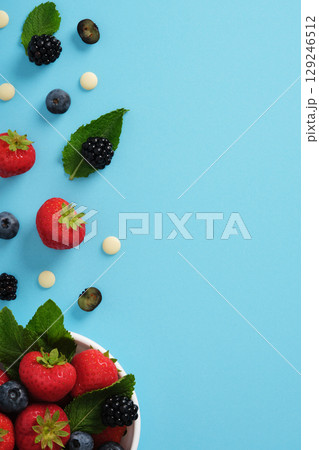 Fragment of white bowl with strawberries, blueberries, blackberries, mint leaves, and white chocolate on blue background. Space for text. Fragment of white bowl with strawberries, blueberries, blackberries, mint leaves, and white chocolate on blue background. Space for text. 129246512