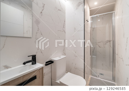 Modern bathroom with marble walls, a glass shower, and a sleek sink. The design is minimalist and contemporary, featuring neutral colors and clean lines. Modern bathroom with marble walls, a glass shower, and a sleek sink. The design is minimalist and contemporary, featuring neutral colors and clean lines. 129246585