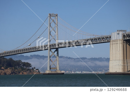 吊り橋と島と青い海と霧のかかる山と海岸の街並みと青空のサンフランシスコの風景 129246688