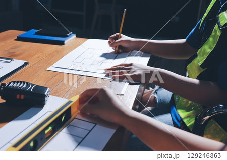 Closeup of team of industrial engineers meeting analyze machinery blueprints consult project on table in manufacturing factory. Working in manufacturing plant or production plant. 129246863