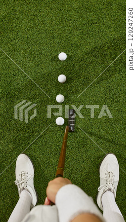 Top view of golfer feet and putter with three balls aligned on green turf 129247260