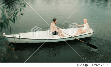 Man and woman laughing and splashing water while rowing boat on river Man and woman laughing and splashing water while rowing boat on river 129247307
