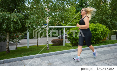 Woman jogging in black activewear through green city park zone 129247362