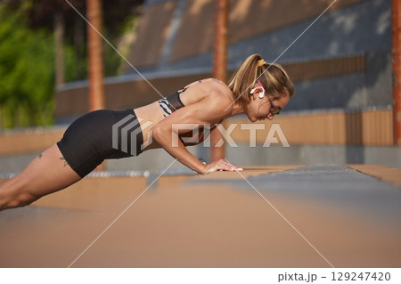 Woman executing push-ups outside on a bright day with concentration and resolve 129247420