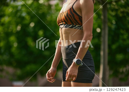 Fit woman in zebra sports bra and shorts standing in park with toned abs Fit woman in zebra sports bra and shorts standing in park with toned abs 129247423