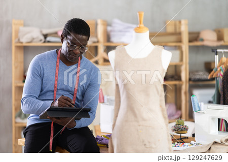 African American man tailor creates sketch of dress on tablet African American man tailor creates sketch of dress on tablet 129247629