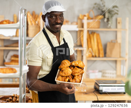 Portrait of joyful man baker with croissants 129247636