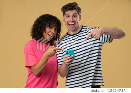 Interracial Couple Pointing to Mobile.Woman Man Smiling With Smartphone on Beige 129247844