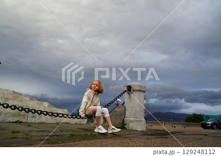 Child Relaxing on Urban Chain Fence with Overcast Sky Child Relaxing on Urban Chain Fence with Overcast Sky 129248112