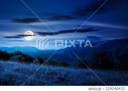 mountain landscape with forest on the hill in autumn at night. beautiful view in to the rural valley in full moon light. alpine countryside scenery under sky with clouds mountain landscape with forest on the hill in autumn at night. beautiful view in to the rural valley in full moon light. alpine countryside scenery under sky with clouds 129248412
