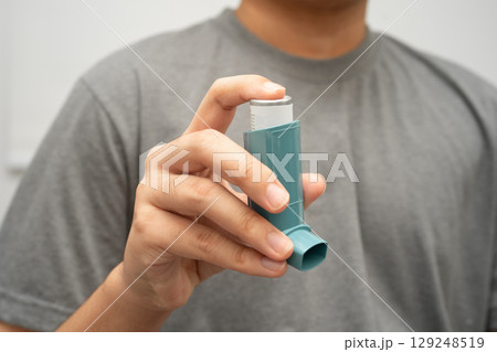 Asthma and chronic obstructive pulmonary disease COPD, Asian young man using metered dose inhaler MDI. 129248519