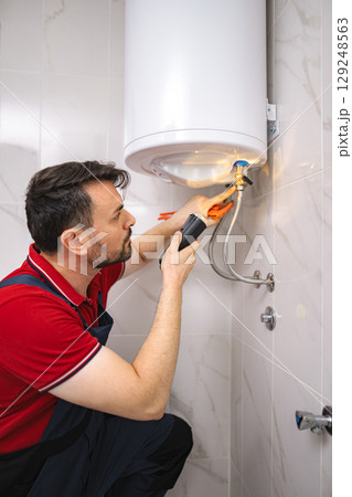 Professional plumber working on a water heater using a flashlight and pliers Professional plumber working on a water heater using a flashlight and pliers 129248563