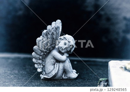 Vintage dirty statue angel on tomb stone in old cemetery.  Small winged angelic figurine on dark grave yard 129248565