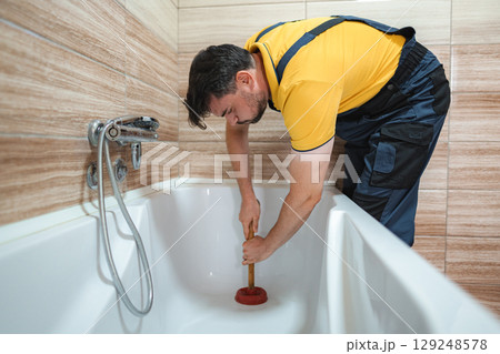 Plumber working to unclog bathtub drain using plunger 129248578