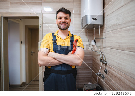 Portrait of smiling plumber holding pipe wrench in bathroom 129248579