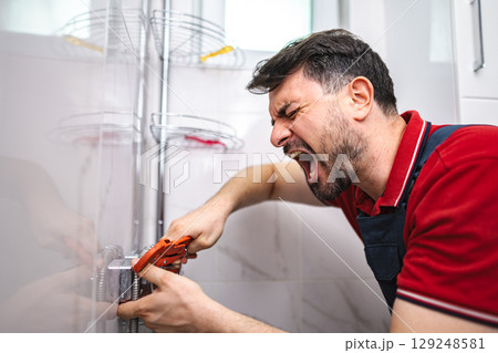 Frustrated plumber screaming while tightening pipe in bathroom Frustrated plumber screaming while tightening pipe in bathroom 129248581
