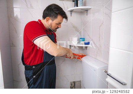 Plumber repairing toilet cistern in bathroom using pliers Plumber repairing toilet cistern in bathroom using pliers 129248582