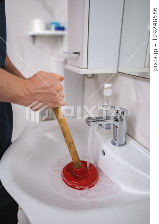 Plumber using plunger in bathroom sink 129248586