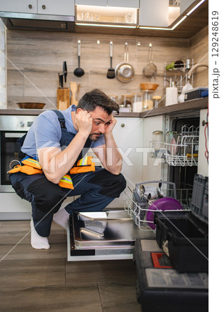 Technician looking stressed while repairing dishwasher in kitchen 129248619