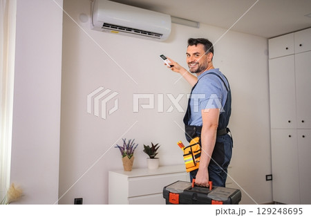 Smiling technician testing an air conditioner with a remote control 129248695