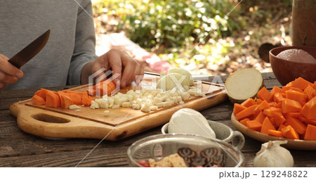 Fresh cut carrot preparation outdoors with various vegetables on wooden cutting board, meal prep in natural setting with vibrant colors and rustic charm 129248822