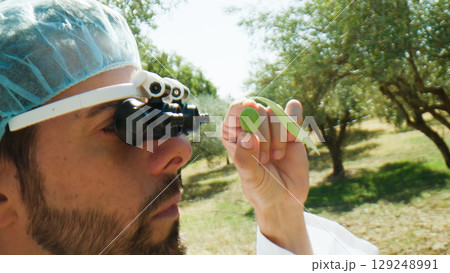 Agronomy scientist looking at an olive with special glasses 129248991