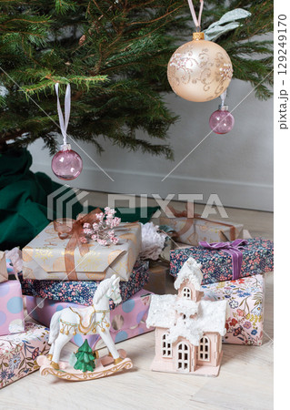 Vibrant pink and purple gift boxes with shiny ribbons rest under a Christmas tree adorned with glowing lights, creating a playful and joyful festive scene Vibrant pink and purple gift boxes with shiny ribbons rest under a Christmas tree adorned with glowing lights, creating a playful and joyful festive scene 129249170