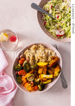 A nutritious breakfast showcases a bowl of quinoa accompanied by vibrant baked sweet potatoes, carrots, zucchini, beans, and turmeric chicken, paired with a fresh salad on the side 129249171
