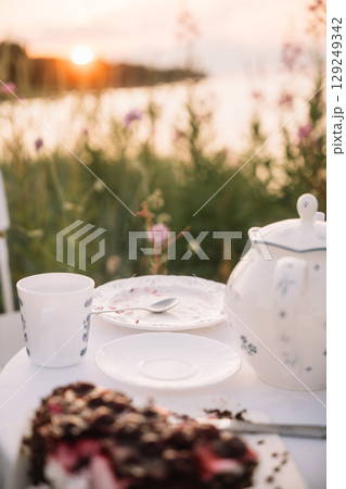 Relaxing tea time by the lakeside during sunset with dessert and floral surroundings Relaxing tea time by the lakeside during sunset with dessert and floral surroundings 129249342