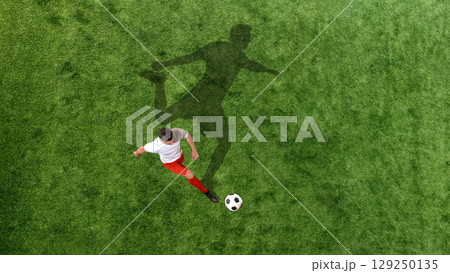 Contemporary collage of soccer player about to kick ball with exaggerated shadow cast across green field 129250135
