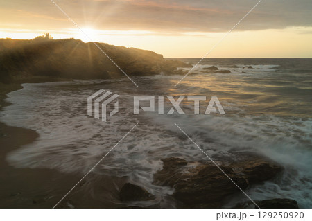 Sea waves crash against rocks at sunset, highlighting climate change impact on coastal ecosystems Sea waves crash against rocks at sunset, highlighting climate change impact on coastal ecosystems 129250920