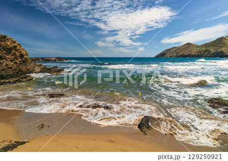 Churning waves hit the sandy shore under a bright sky with scattered clouds during a warm day Churning waves hit the sandy shore under a bright sky with scattered clouds during a warm day 129250921