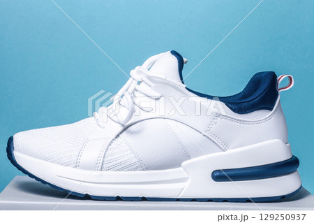 vWhite men's sneaker on blue background. Modern sports casual shoes. New running unisex footwear, side view vWhite men's sneaker on blue background. Modern sports casual shoes. New running unisex footwear, side view 129250937