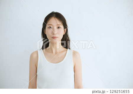 肌に触れてスキンケアする若い女性の笑顔 – 自然光・白背景 129251655