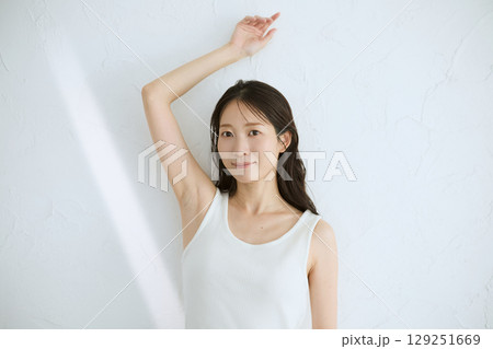 肌に触れてスキンケアする若い女性の笑顔 – 自然光・白背景 129251669