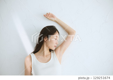 肌に触れてスキンケアする若い女性の笑顔 – 自然光・白背景 129251674