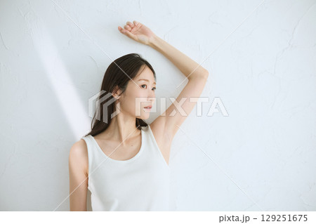 肌に触れてスキンケアする若い女性の笑顔 – 自然光・白背景 129251675