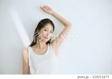 肌に触れてスキンケアする若い女性の笑顔 – 自然光・白背景 129251677