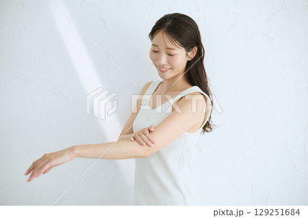 肌に触れてスキンケアする若い女性の笑顔 – 自然光・白背景 129251684