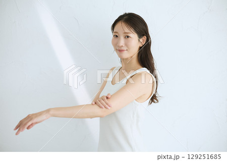 肌に触れてスキンケアする若い女性の笑顔 – 自然光・白背景 129251685